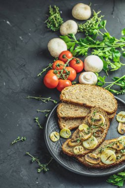 Lezzetli ev yapımı tam tahıl Çavdar ekmek tost ile dilimlenmiş mantar champignon ve soğan siyah seramik kaplama, otlar ve siste, karanlık beton masa yüzeyi, kopya alanı üzerinde kesme kızarmış.