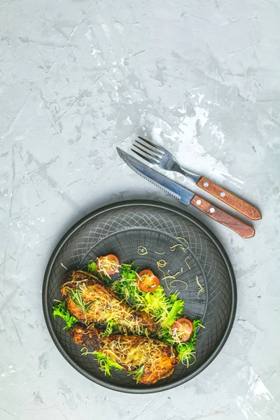 Pečené kuřecí stehno v černý keramický talíř s rajčaty — Stock fotografie