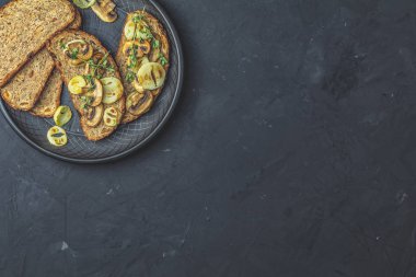 Lezzetli ev yapımı tam tahıl Çavdar ekmek tost ile dilimlenmiş mantar champignon ve soğan siyah seramik kaplama, otlar ve siste, karanlık beton masa yüzeyi, üstten görünüm, kopya alanı üzerinde kesme kızarmış