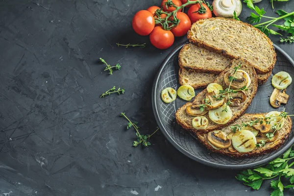 Lezzetli ev yapımı tam tahıl Çavdar ekmek tost ile dilimlenmiş mantar champignon ve soğan siyah seramik kaplama, otlar ve sebze, karanlık beton masa yüzeyi, kopya alanı üzerinde kesme kızarmış.