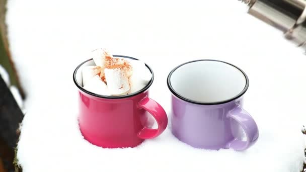 カップに注いでホット チョコレート ピンクと紫の つのカップに包まれた庭の雪に覆われたテーブルの上の居心地の良い冬ピンク スカーフでマシュマロとホット チョコレート — ストック動画