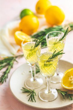 Geleneksel İtalyan ev yapımı limon alkol içki likör limoncello adet limon ve biberiye bitki pembe üzerinde şeftali veya Mercan rengi taş beton yüzey