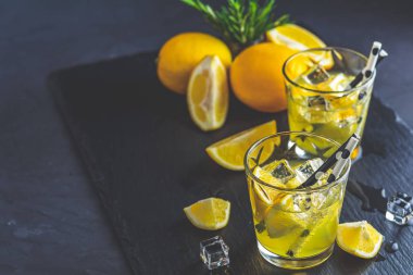 Limon alkol siyah taş beton yüzeyinde buz, limon ve biberiye bitki ile kokteyl içmek. Geleneksel İtalyan ev yapımı limon alkol içki likör limoncello.