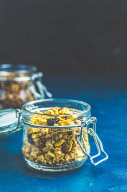 Çilek ile organik granola iki açık cam kavanoz, Hindistan cevizi cips ve koyu mavi beton masa yüzeyine tohum.