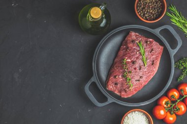 Taze çiğ et Dana biftek siyah tavada pişirme baharat, kekik, biberiye ve domates koyu arka plan, üstten görünüm için malzemelerle kopya alanı sizin için metin.