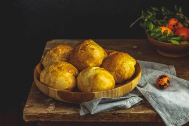 Mutlu Paskalya kartpostal ahşap plaka ile ayakta ev yapımı buns ile renkli sarı turuncu yumurta ile Bıldırcın yumurta ve keten masa örtüsü yeşil dallarda. Kopya alanı, karanlık rustik tarzı.