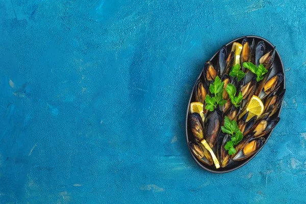 Zeevruchten mosselen met citroen en peterselie in zwarte metalen plaat — Stockfoto