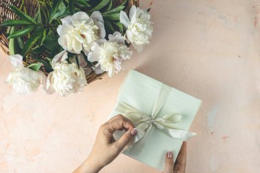 Kadın hediyesini açıyor, üst manzara. Kadınların elleri, beyaz şakayık çiçeklerin arasındaki hediye paketini açmak için kurdele çeker..