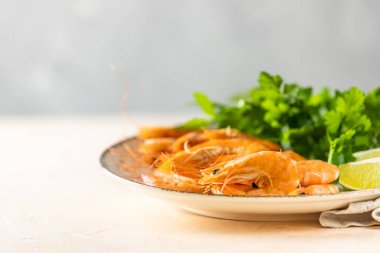 Seramik tabakta kaynatılmış güzel karides maydanoz ve pembe beton masa yüzeyinde limon. Taze deniz ürünleri - karides kuyruğu pişirmeye hazır..