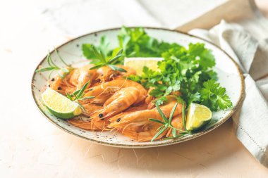 Seramik tabakta kaynatılmış güzel karides maydanoz ve pembe beton masa yüzeyinde limon. Taze deniz ürünleri - karides kuyruğu pişirmeye hazır..