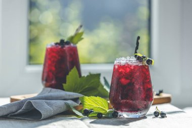 İki bardak soğuk, siyah üzümlü, olgun böğürtlenli ve yeşil yapraklı üzüm suyu pencerenin yanındaki güneşli odada, bahçeli bir masada..