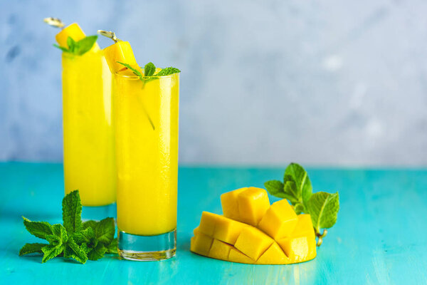 Освежающие летние коктейли из манго, холодного напитка или напитка со льдом на синем сером фоне. Свежий летний холодный коктейль манго или сок с мятой и манго фрукты.