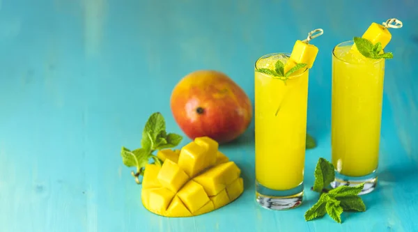 Refreshing summer cocktails made of mango, cold drink or a drink with ice on a blue gray background. Fresh summer ice cold mango cocktail or juice with mint  and mango fruit.