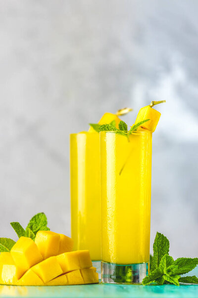 Освежающие летние коктейли из манго, холодного напитка или напитка со льдом на синем сером фоне. Свежий летний холодный коктейль манго или сок с мятой и манго фрукты.