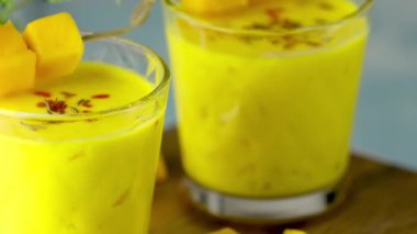 Sarı Hint mangolu yoğurt Mango Lassi ya da zerdeçal ve safranlı smoothie. Sağlıklı probiyotik Hint soğuk yaz içeceği mavi arka planda yavaşça ilerliyor