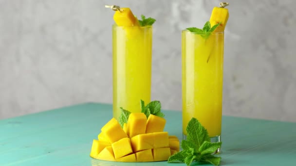 新鲜的夏季冰凉芒果鸡尾酒与薄荷和芒果 新鲜的芒果汁在浅蓝色的背景上缓缓流动 — 图库视频影像