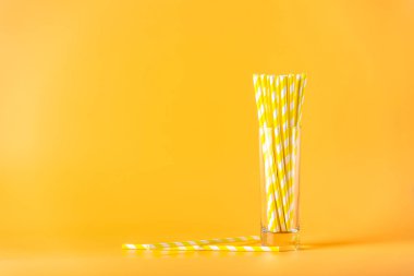 Sarı arka planda sarı şeritli ve fotokopi alanı olan parti için kağıt pipetler içmek. Renkli kağıt harcanabilir eko - yaz kokteylleri için dost pipetler.