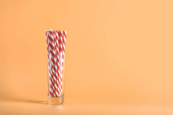 Drinking paper straws for party with red stripes in glass cup on peachy background with copy space. Colorful paper disposable eco - friendly straws for summer cocktails.