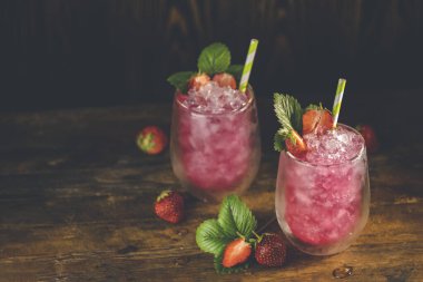 Buzlu çilekli içecek. Tahta turkuaz masa yüzeyinde olgun böğürtlenli iki bardak çilekli içecek. Alkolik, alkolsüz yaz içeceği