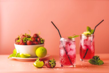 İki bardakta buzlu çilekli mojito kokteyli ve pembe arka planda su damlaları. Kopyalama alanı, yaz tatili ve parti konsepti