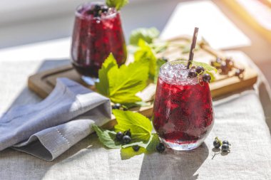 İki bardak soğuk, siyah üzümlü, olgun böğürtlenli ve yeşil yapraklı üzüm suyu pencerenin yanındaki güneşli odada, bahçeli bir masada.