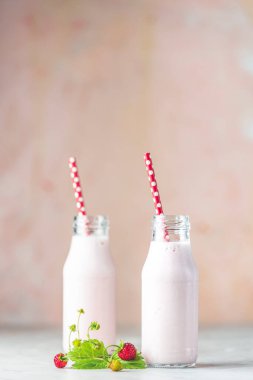 Bottles with delicious strawberry milkshake or smoothie with branch of wild strawberry on table and pink background.	