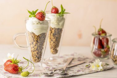 Two glass of healthy breakfast with granola and greek yogurt decorated by mint and raw strawberry served on white wooden background.	