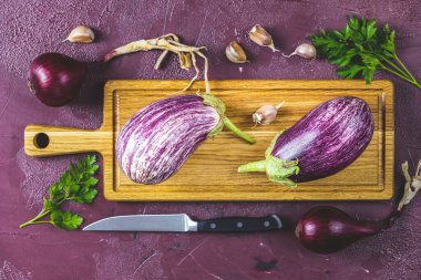 Tahta kesme tahtasındaki farklı taze patlıcanlar. Yeşil ev yaşam tarzı ve geçimlik tarım ürünleri kavramı, düz yerde bordo beton yüzey, kopyalama alanı