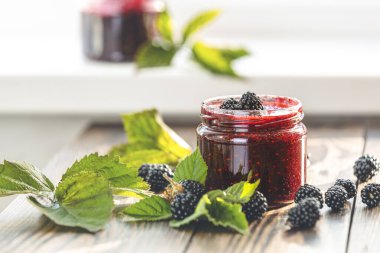 Ahşap arka planda cam kavanozda taze ev yapımı böğürtlen reçeli. Yanında bir sürü taze meyve var..