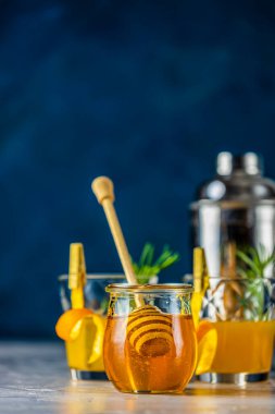 İki bardak ballı burbon kokteyli. Biberiye şurubu ya da ev yapımı viski kokteyli. Portakal ve biberiye süslemesi portakal kabuğu, bir kavanoz bal ve barmen aletleri.