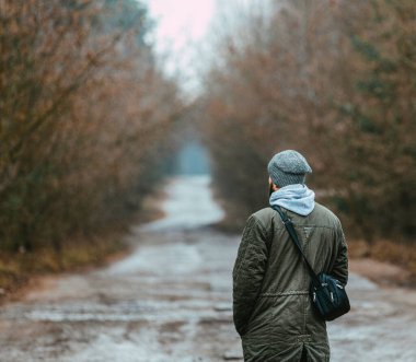 Sıcak ceketli ve örgü şapkalı bir adamın sisli bir ormanda dikiliş görüntüsü..