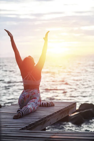 woman playing yoga pose on beach pier against sun rising sky