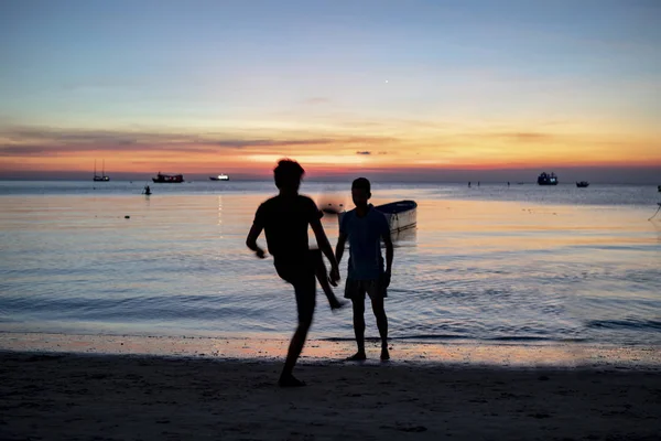 つのシルエット男夕焼け空と海のビーチで遊ぶサッカー — ストック写真