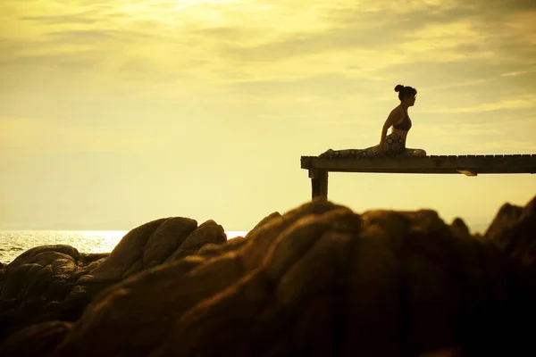 在海滩码头对美丽的太阳升起的天空的妇女演奏瑜伽姿势 — 图库照片