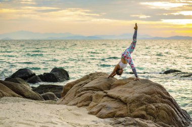 Yoga poz deniz kumsalda güzel güneş doğuyor gökyüzü karşı oynayan kadın