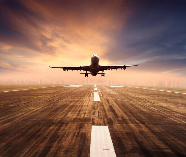 air plane flying over airport runway with city scape and sunset sky background