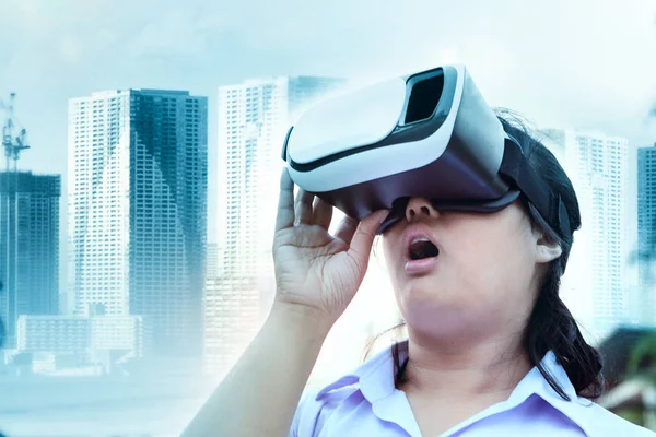 younger woman wearing virtual reality glasses with surprising face standing outdoor against modern city building  background