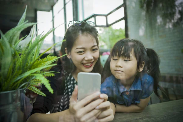 自宅のリビングルームで携帯電話を見ているアジアの女性と少女は — ストック写真
