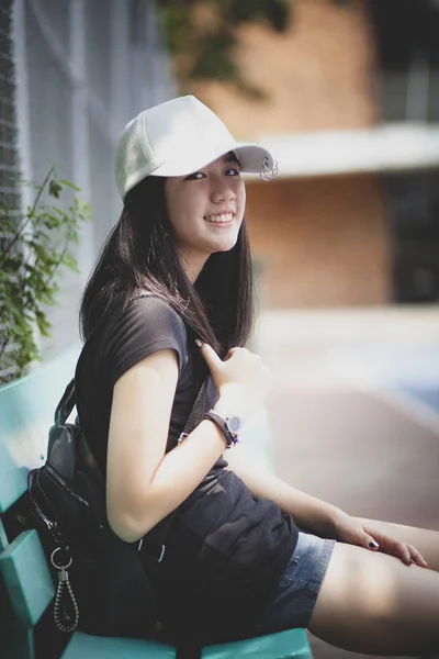 Portrét asijského teenagera s bílou čapkou sedící venku a — Stock fotografie