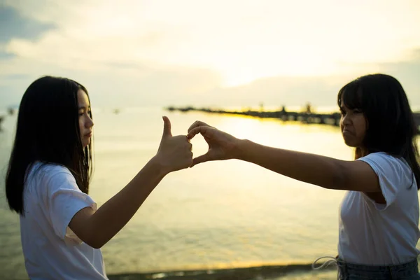 Dos asiático adolescente jugando en mar playa contra hermosa puesta de sol —  Fotos de Stock