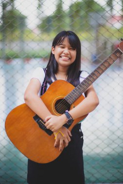Akustik gitar çalan Asyalı ergen dişlek gülen surat 