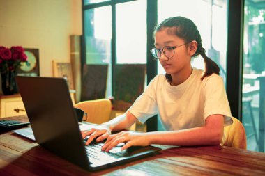 Asyalı genç evde oturuyor ve bilgisayarda yazı yazıyor.