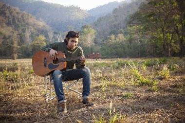 Asyalı adam olay yerinde akustik gitar çalıyor.