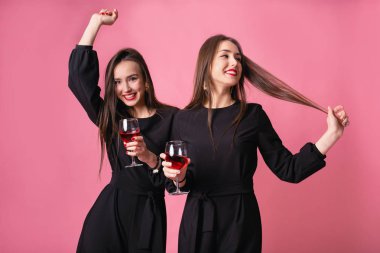 Two attractive women in night dress drinking wine isolated on a plastic pink background