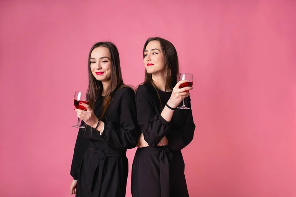 Two attractive women in night dress drinking wine isolated on a plastic pink background — Stock Photo, Image