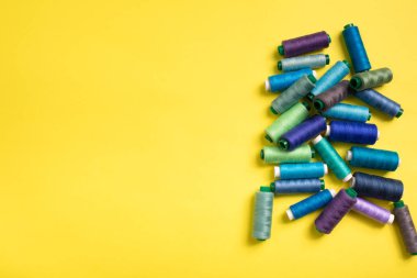 Sarı arka planda renkli iplik bobinleri, dikiş ve terzilik.