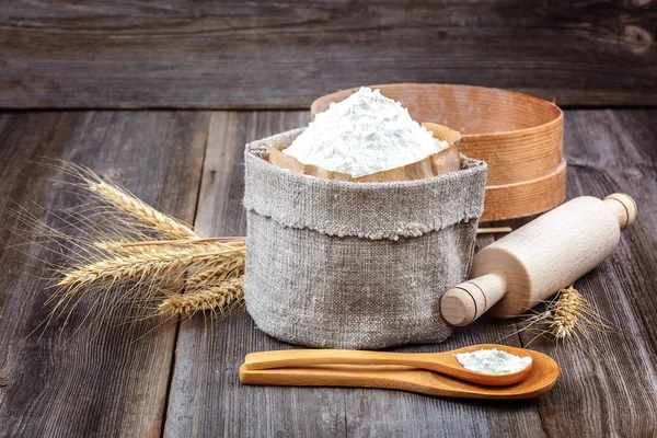 Flour in a canvas bag, wheat ears on a wooden background.