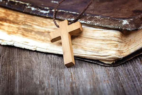 Ancient holy book of a wooden cross on a cord on a wooden background.