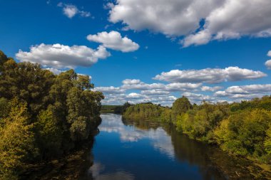Nehir, ağaçlar, çayır mavi gökyüzü beyaz bulutlar ile karşı.