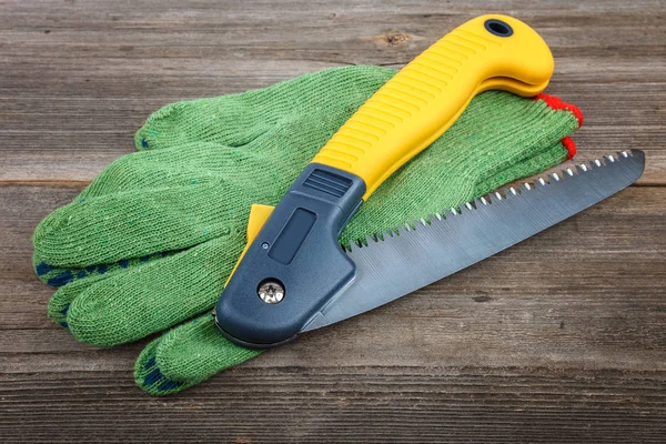Folding garden saw with work gloves on wooden boards.
